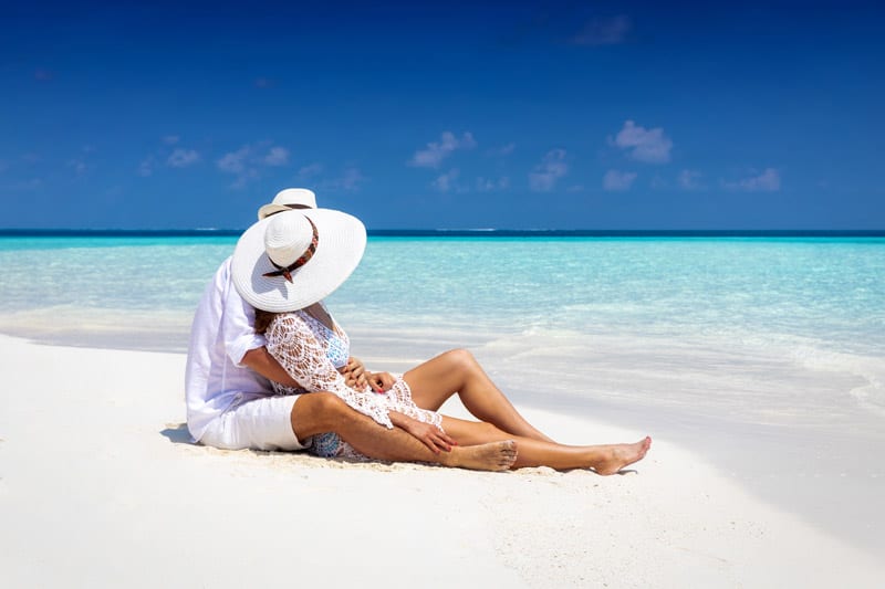 Couple sits hugging deserted tropical beach Maldives