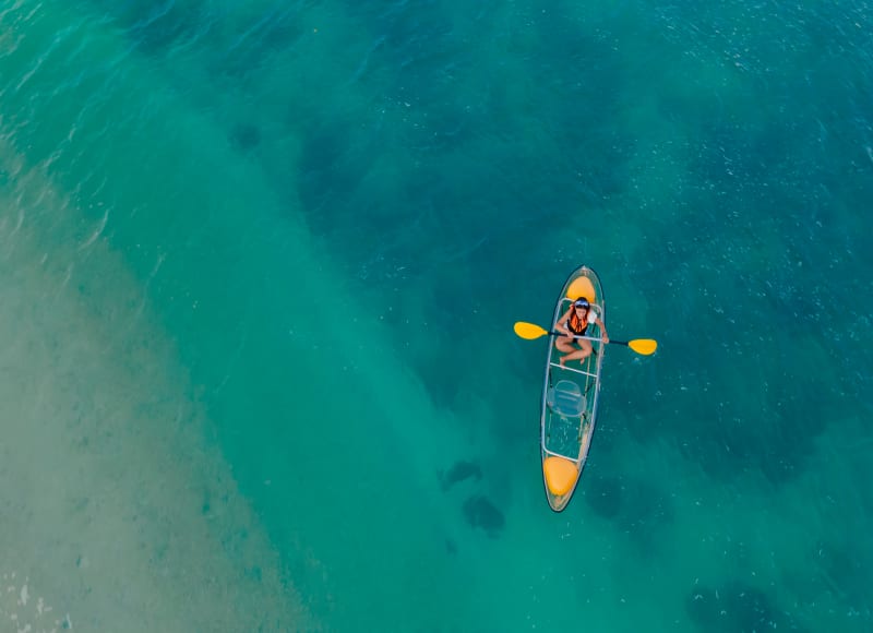 A resort guest floats over the water in a transparent kayak